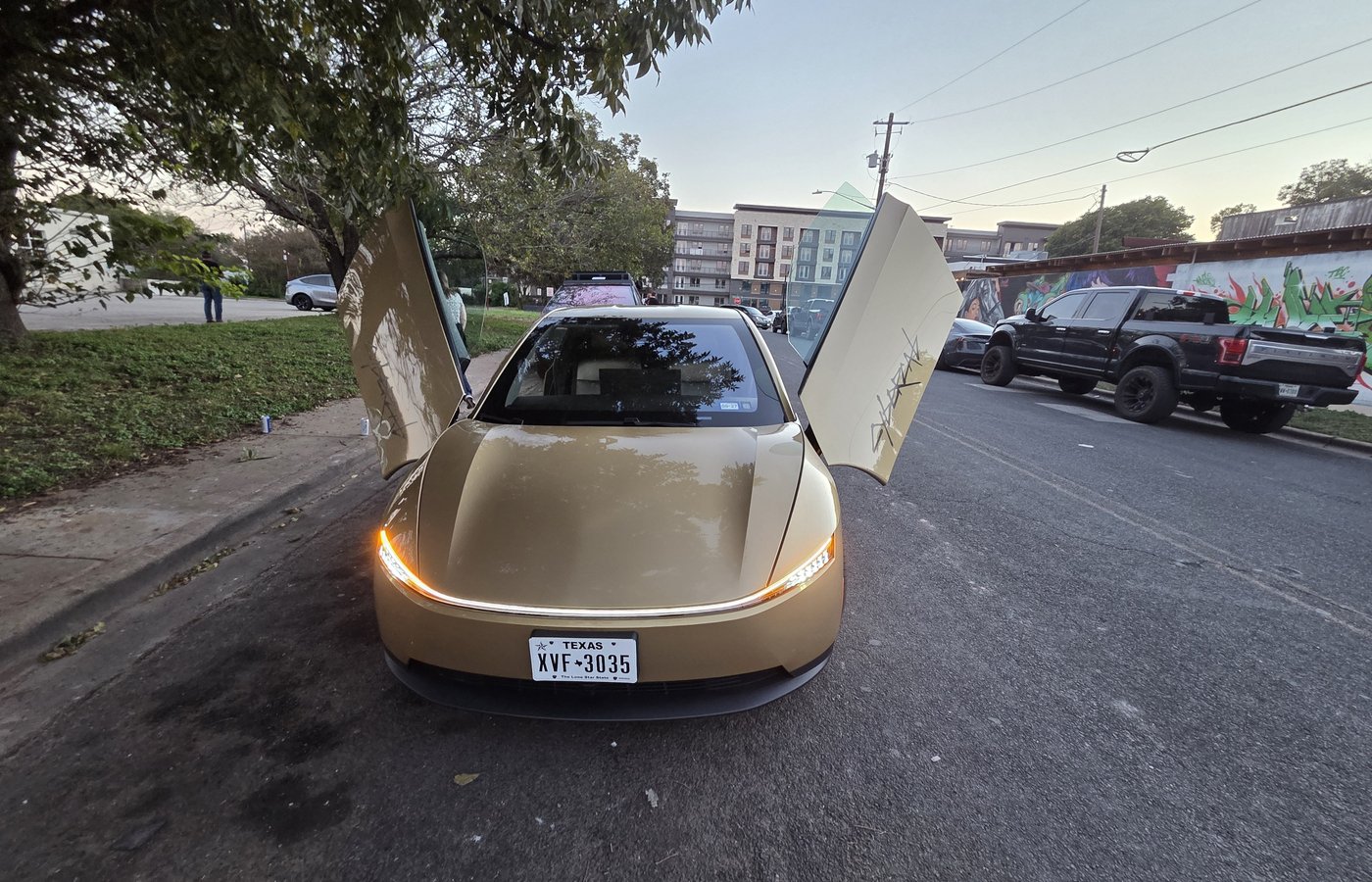 A gold Tesla Cybercab parked at night beside event lighting in Austin