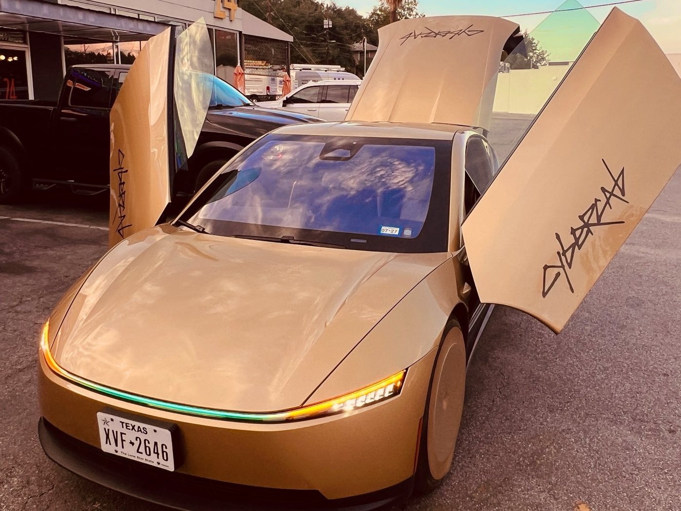 A gold Tesla Cybercab with both butterfly doors open and its light bar glowing, parked on an Austin street