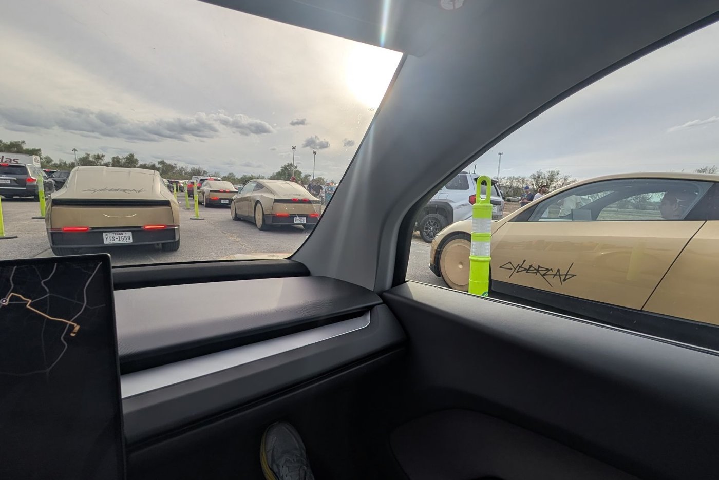 Gold Tesla Cybercabs lined up outside Circuit of the Americas, seen through the window of a Tesla Robotaxi