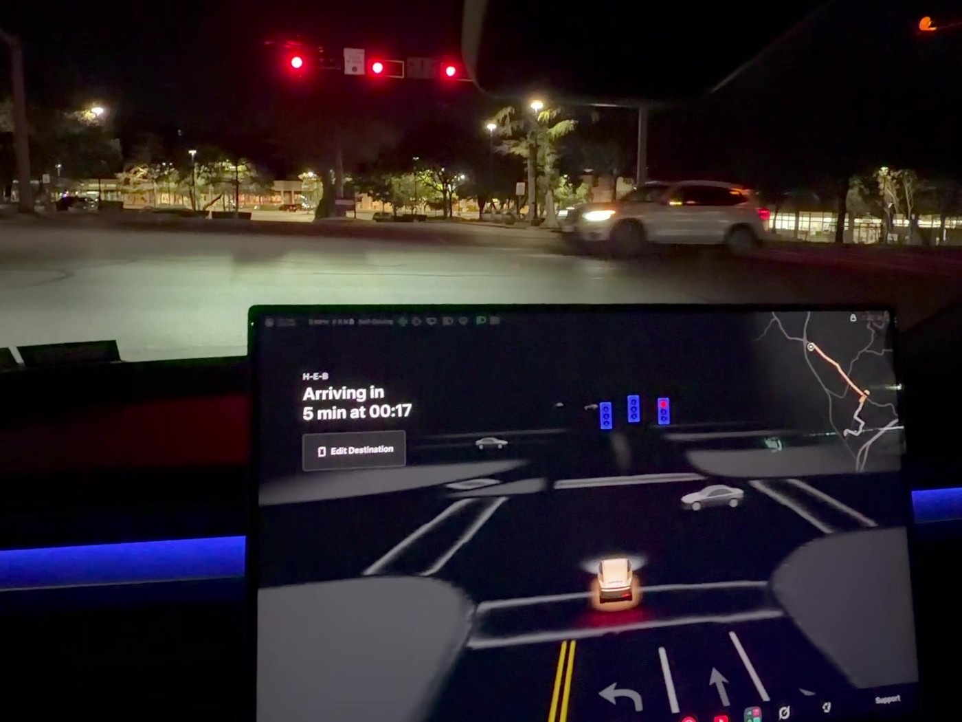 Inside a Cybercab after midnight: the cabin screen shows arrival at H-E-B at 00:17 as the car waits at a blinking red signal. Image via @WorldlyReviewer / X
