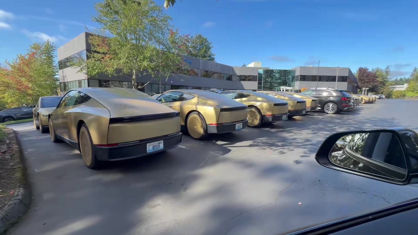 A row of gold Tesla Cybercabs with Washington plates parked outside an office building in Bellevue, Washington