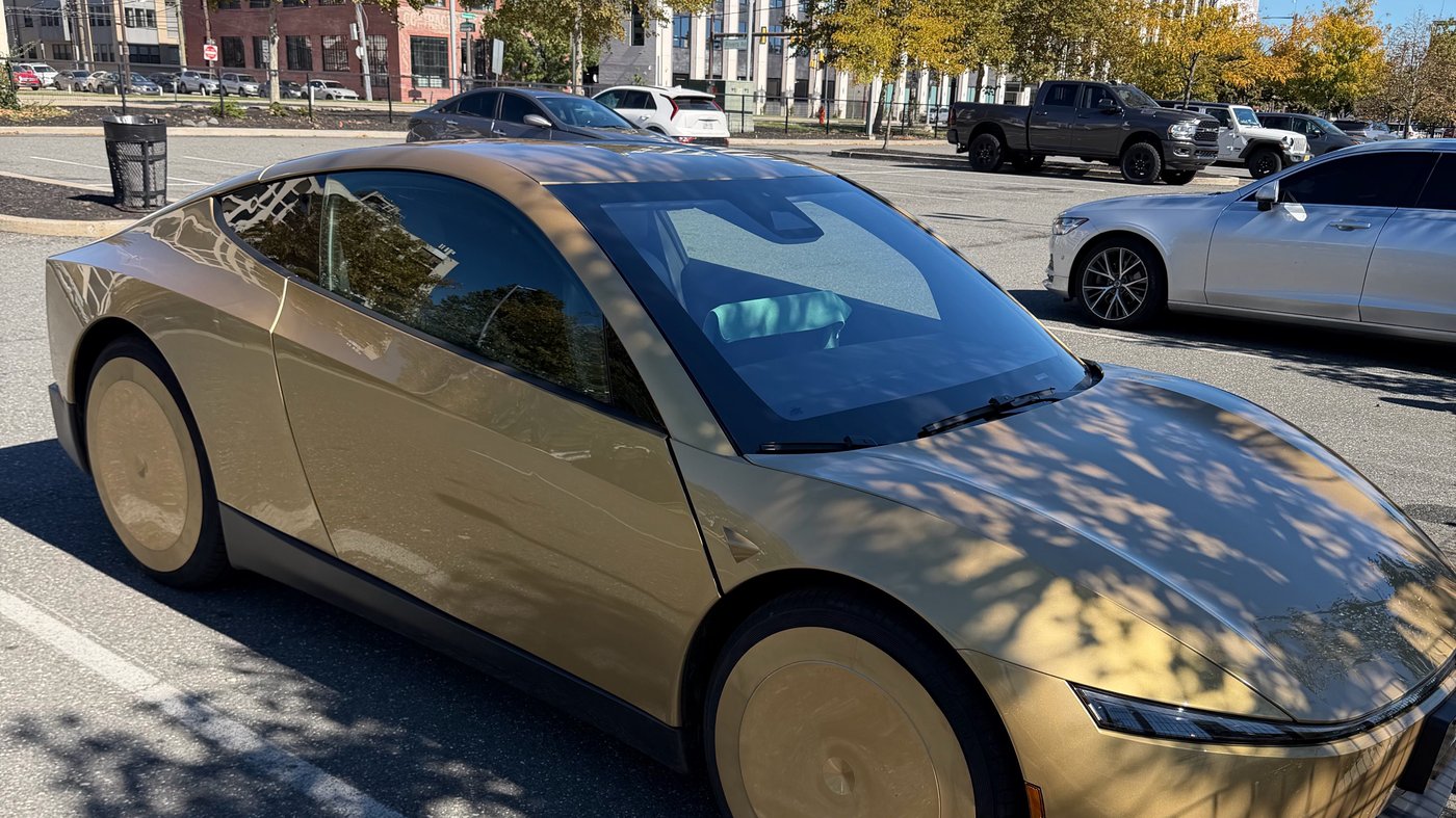 A gold Tesla Cybercab parked in a sunny lot in front of a modern building in Philadelphia