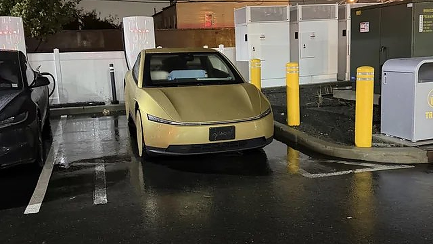 A gold Tesla Cybercab parked at a Supercharger stall on a wet night at a Wawa in North Bergen, New Jersey, beside a black Tesla