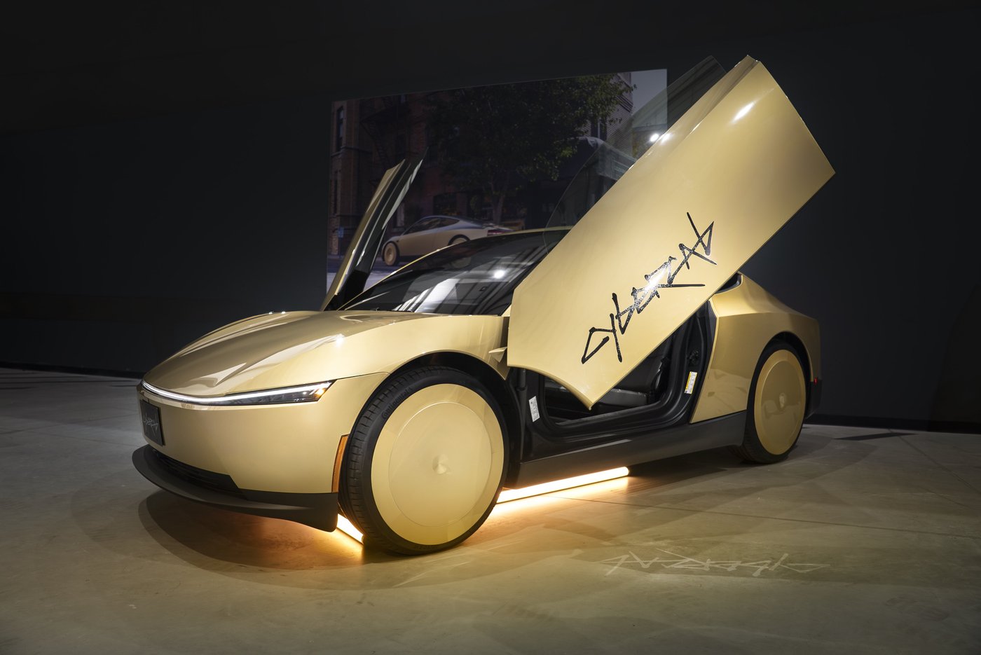 A gold Tesla Cybercab with its butterfly doors raised on a lit display floor