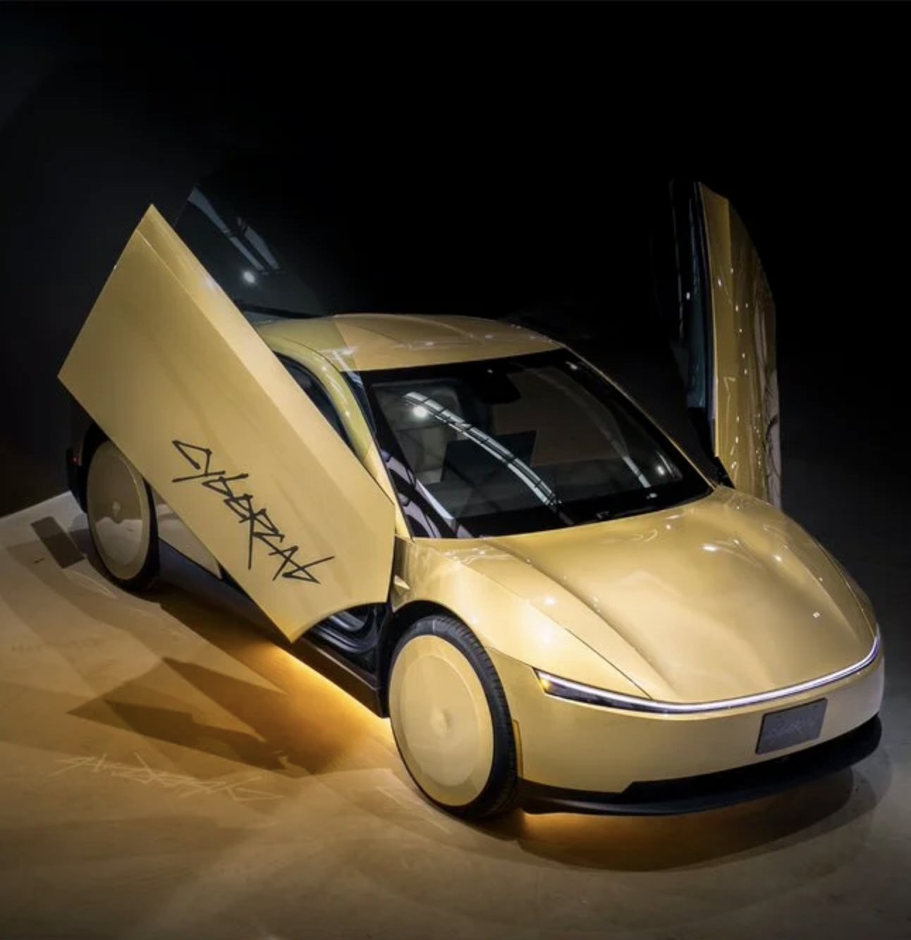 A gold Tesla Cybercab on display under spotlights with both doors raised