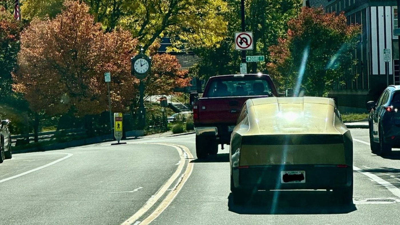 A gold Tesla Cybercab seen from behind on a tree-lined street in autumn sunshine
