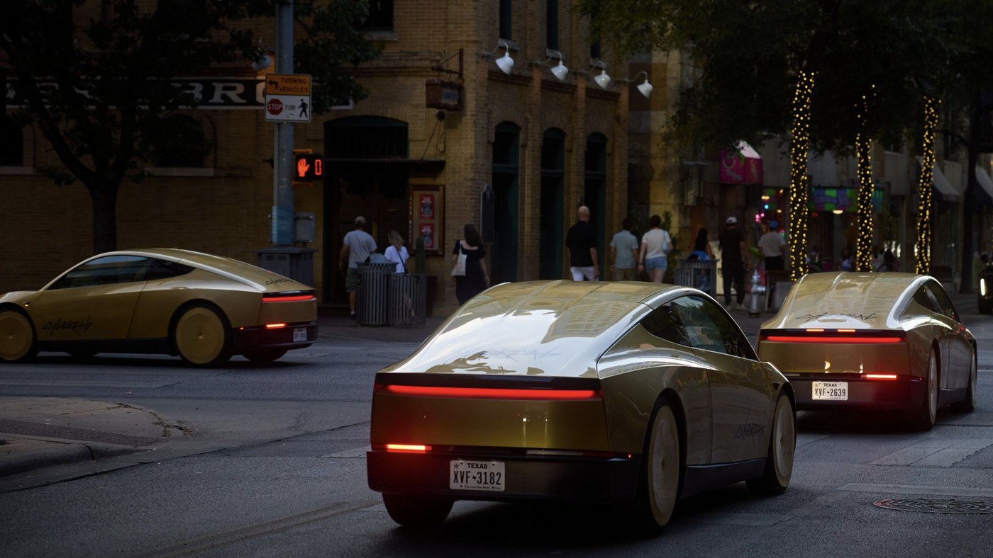 Gold Tesla Cybercabs driving along a city street at dusk, with pedestrians on the pavement and shopfronts behind them