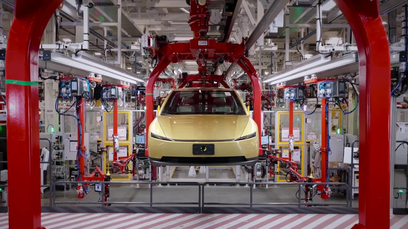 A gold Tesla Cybercab held by a red overhead cradle on the Giga Texas assembly line