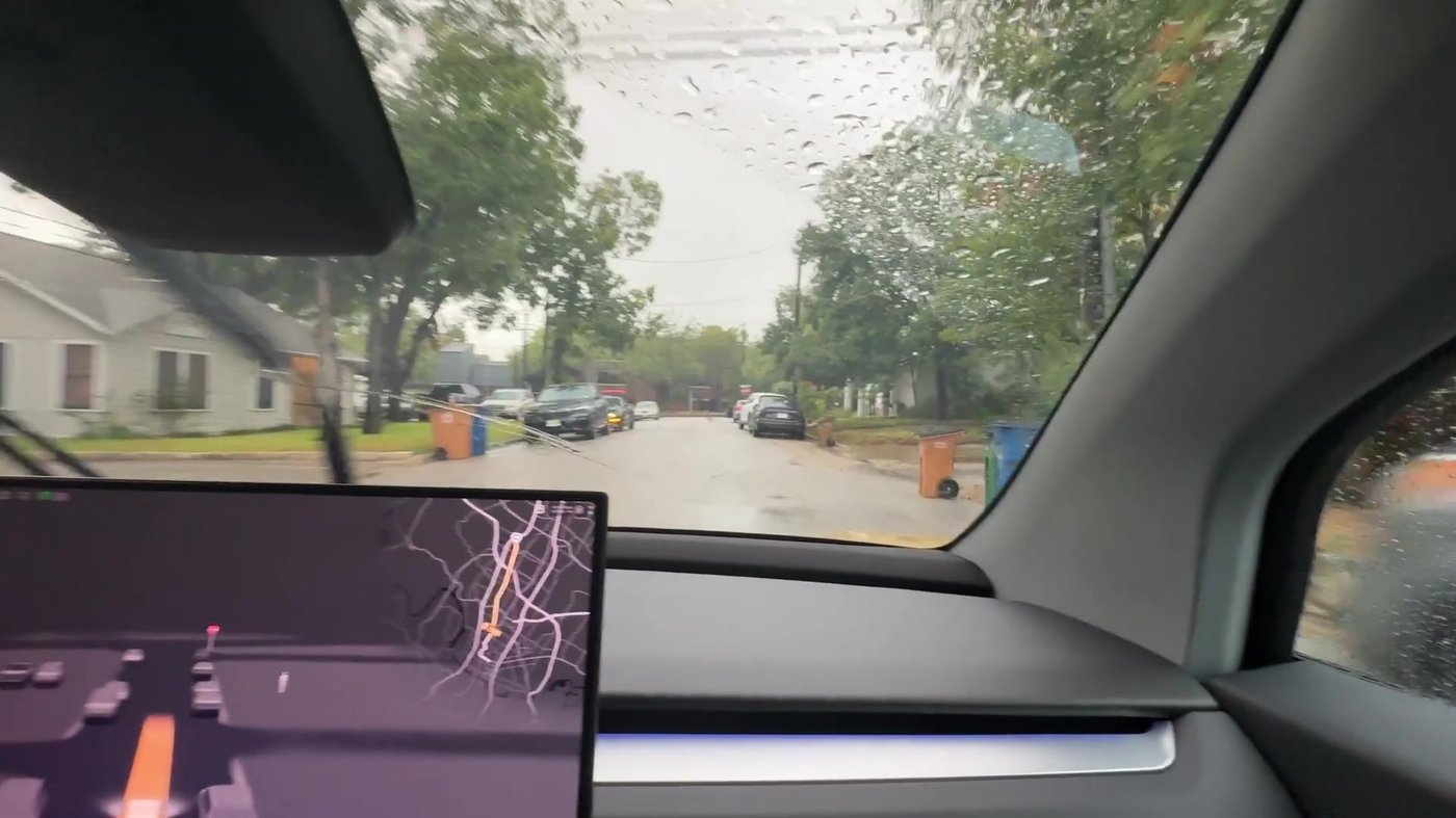 The view from inside a Cybercab on a rainy Austin street, with the ride screen on the dashboard