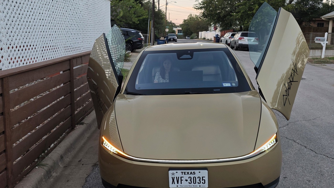 A gold Tesla Cybercab with butterfly doors open on a residential street in Texas, Texas plate XVF-3035