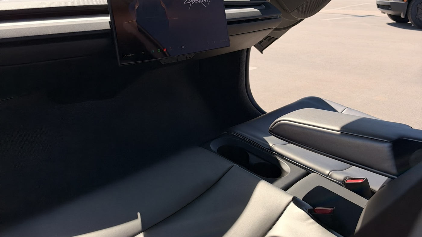 The two-seat bench and center screen inside a Tesla Cybercab, seen through its raised butterfly door