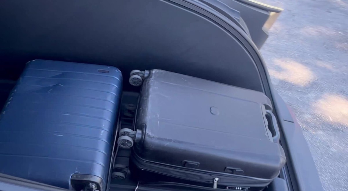 Two hard-shell suitcases seated in an open Cybercab trunk, a real-world look at the cargo bay Tesla rates at 20.2 cubic feet. Still via @BLKMDL3 / X