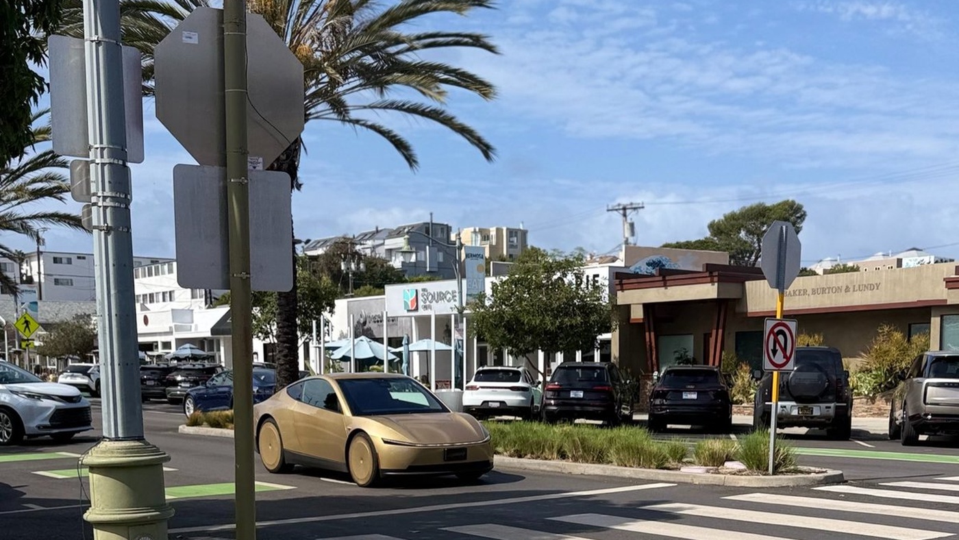 A gold Tesla Cybercab turning through a sunlit street near palm trees in Hermosa Beach