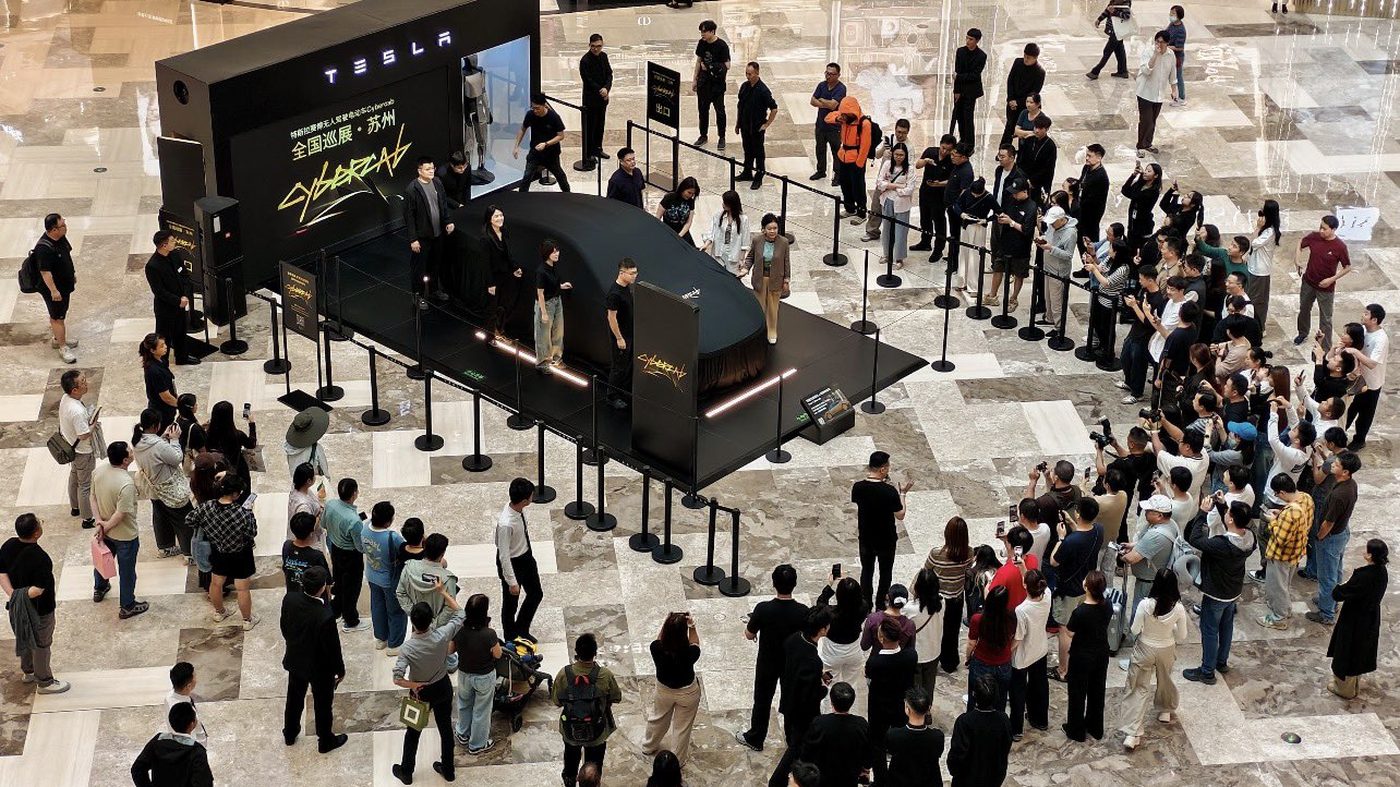 Crowds several rows deep ring a black Tesla stage at Suzhou MixC World as staff prepare to unveil a covered Cybercab