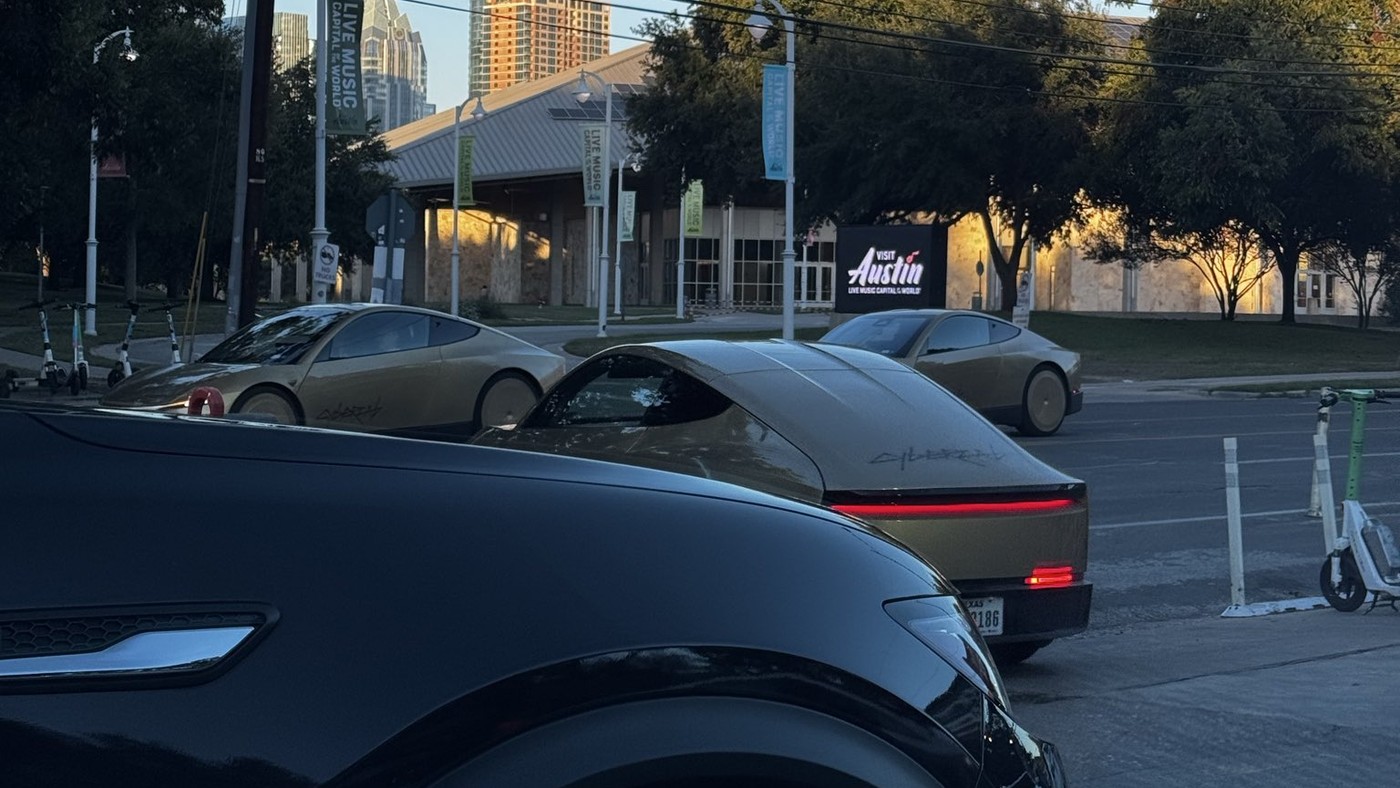Gold Tesla Cybercabs lined up at the curb outside Terry Black's Barbecue in Austin, with a downtown tower in the background