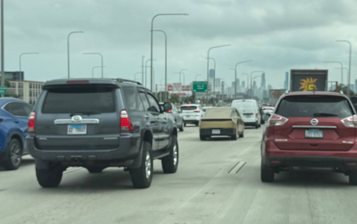 Gold Cybercab in city highway traffic with a skyline ahead.