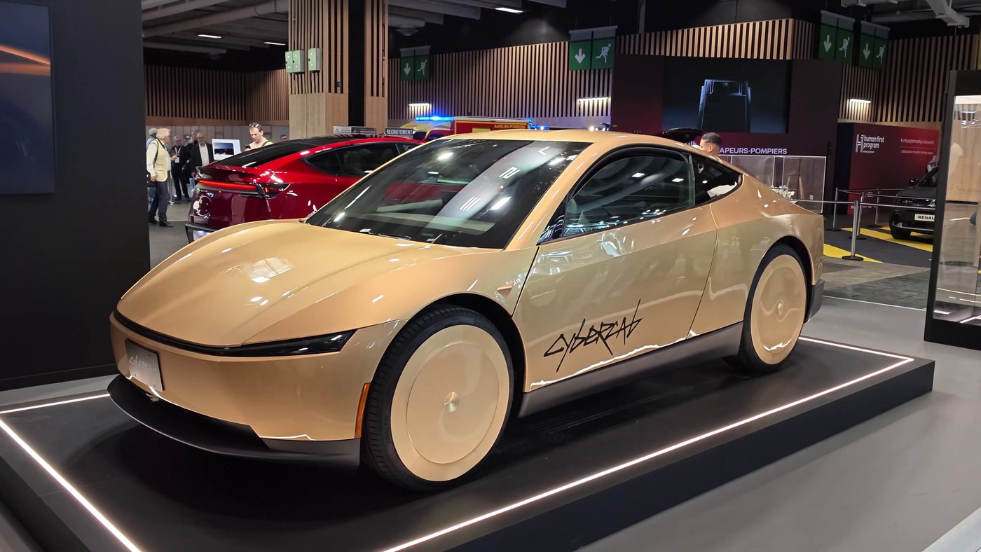 A gold Tesla Cybercab on a lit black plinth on Tesla's stand at the Paris Motor Show, red Teslas behind it