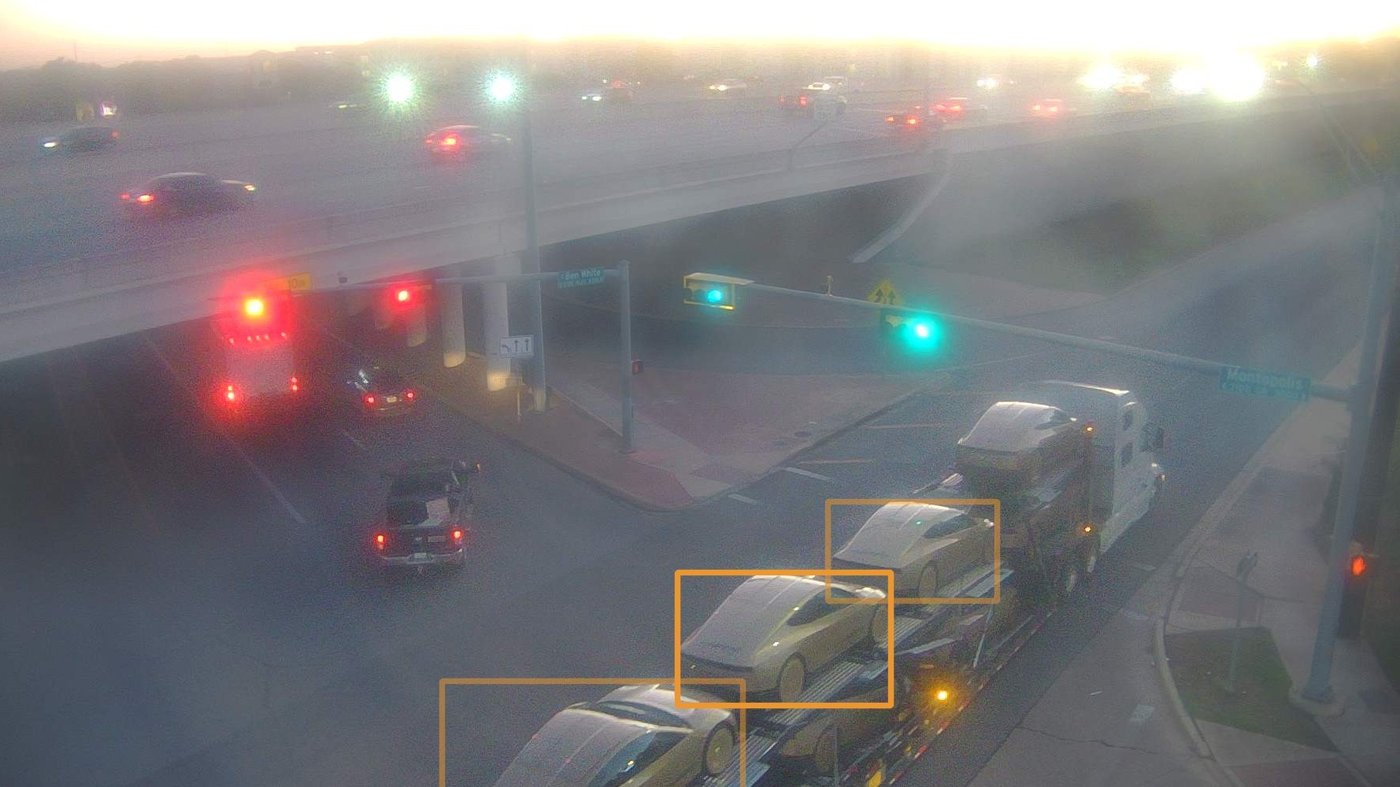A car carrier loaded with Cybercabs travels through an Austin intersection, with tracking boxes drawn around the cars