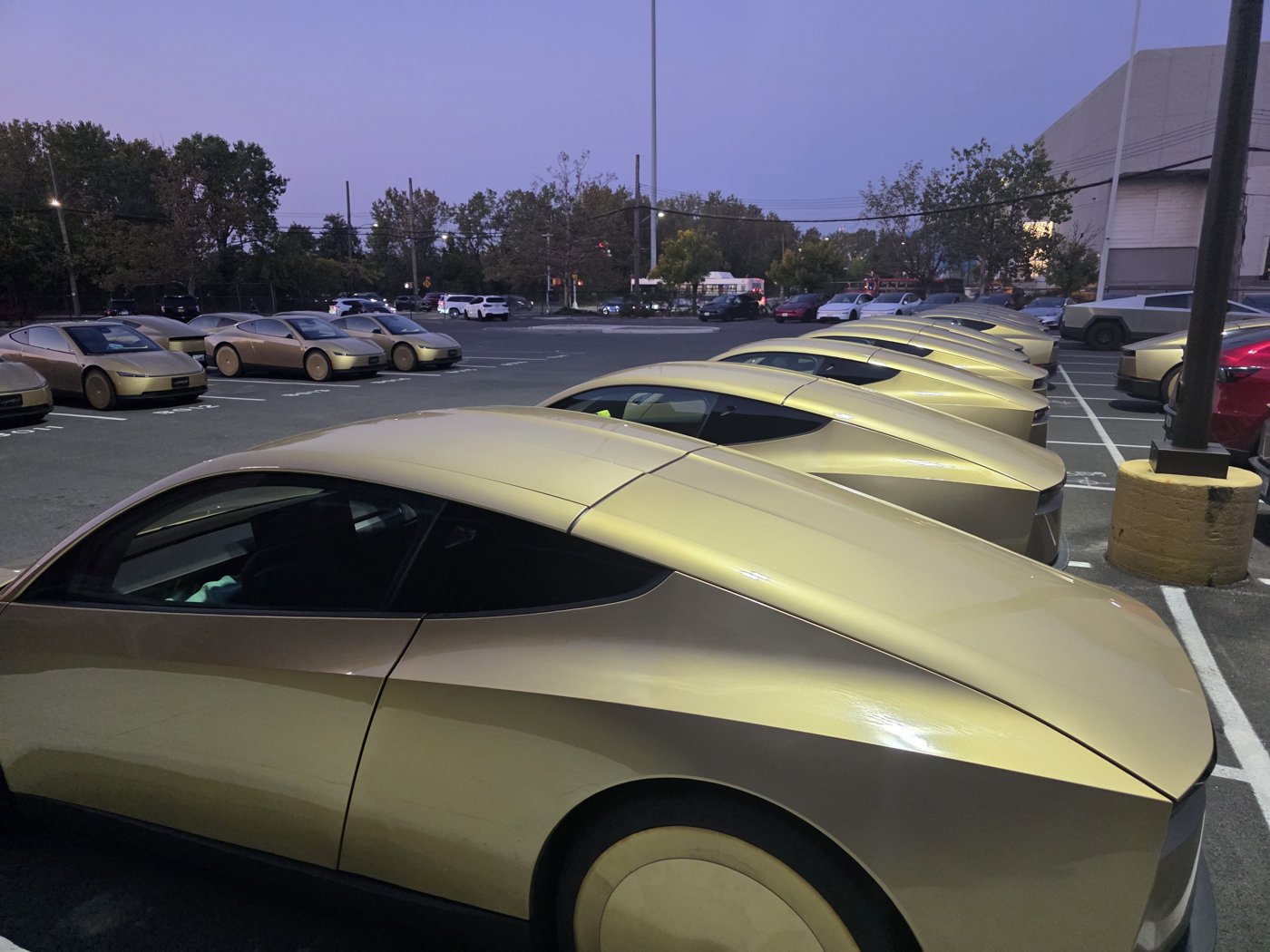 Rows of gold Tesla Cybercabs parked in a lot outside a Tesla building in College Point, Queens, at dusk
