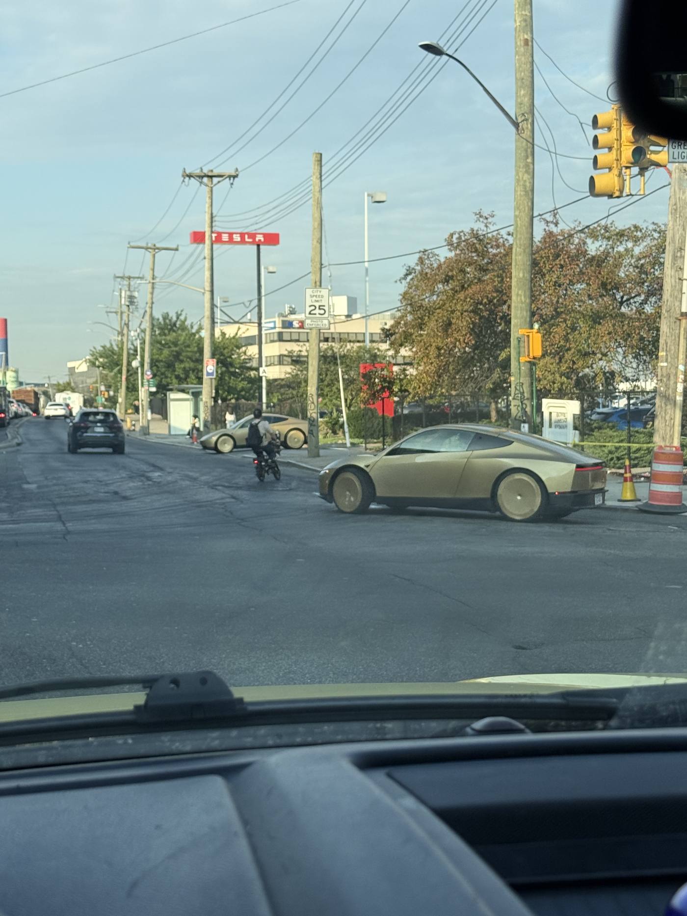 Two gold Cybercabs on the same Queens block near a Tesla sign.