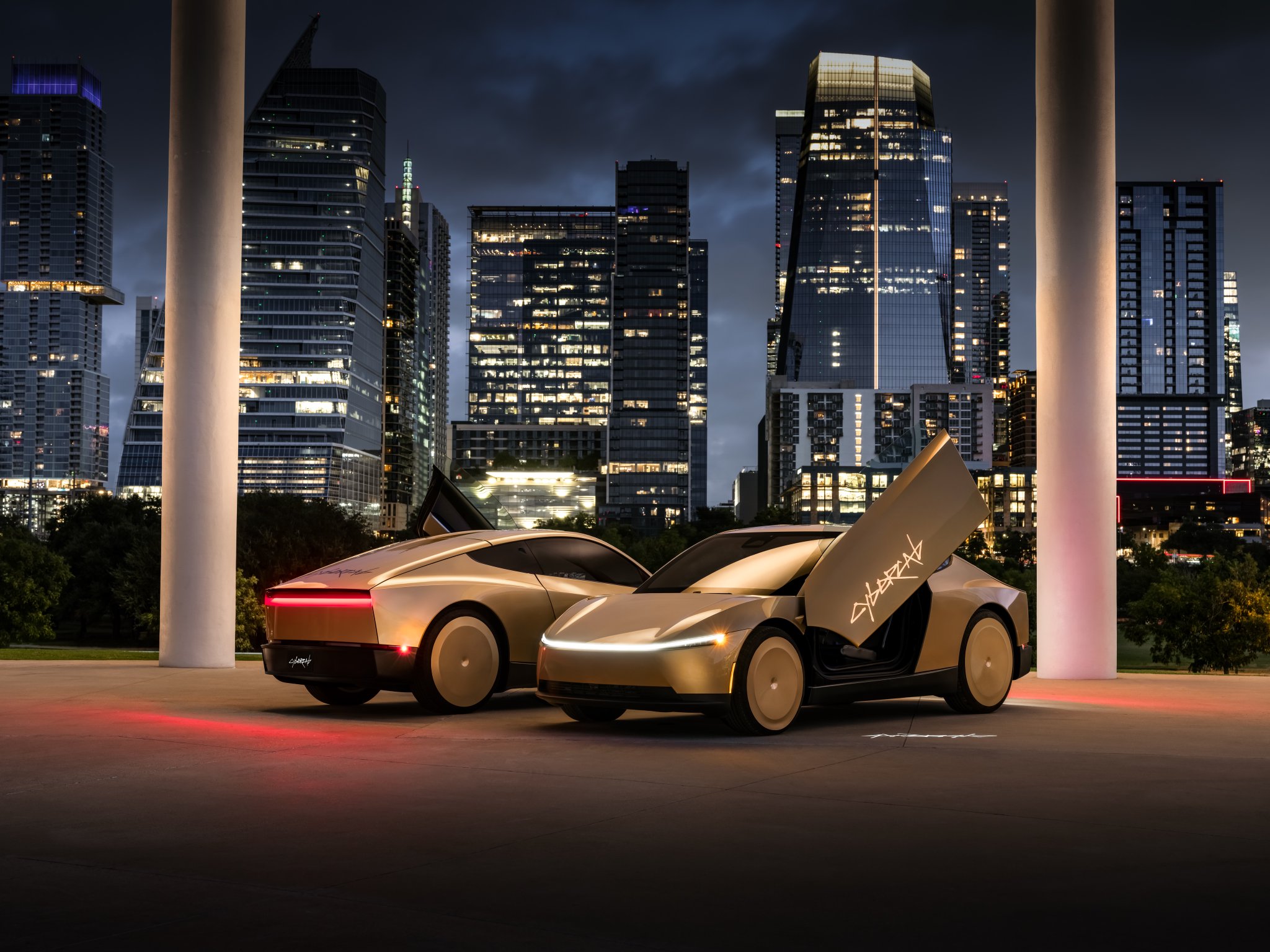 Two gold Tesla Cybercabs parked at night with a gull-wing door open in front of the Austin skyline