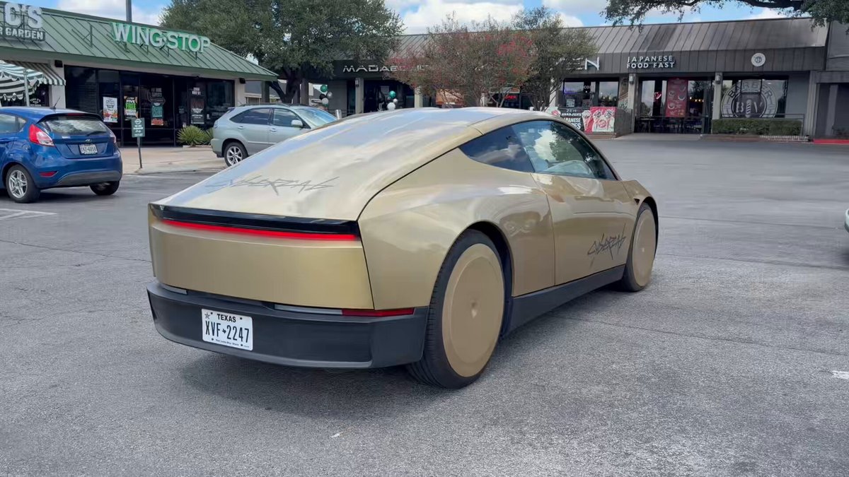 A gold Cybercab on an Austin street with butterfly doors closed and no conventional front grille.