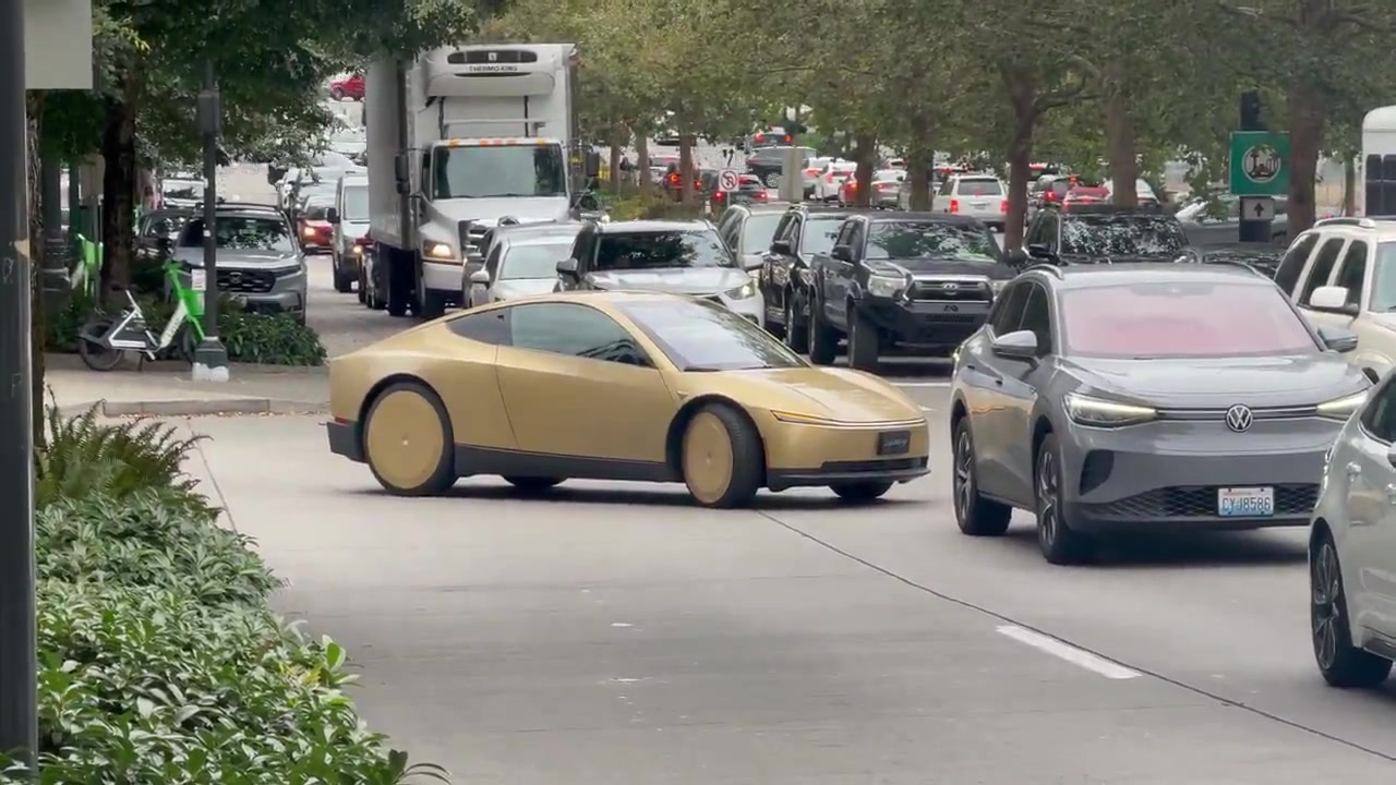 A gold wheel-less Cybercab in South Lake Union traffic beside a Volkswagen ID.4, disc aero covers and no side mirrors.