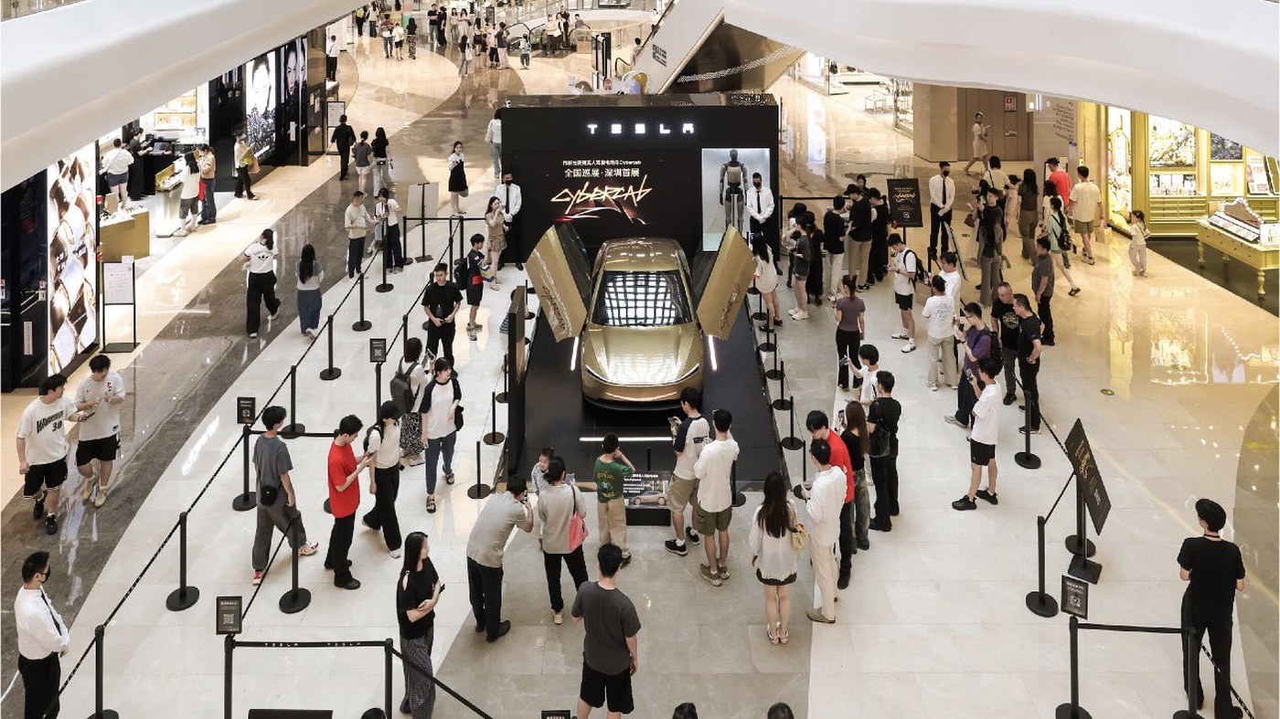Visitors gather around a gold Tesla Cybercab with its butterfly doors raised on a black Tesla stage in the atrium of One Avenue mall in Shenzhen