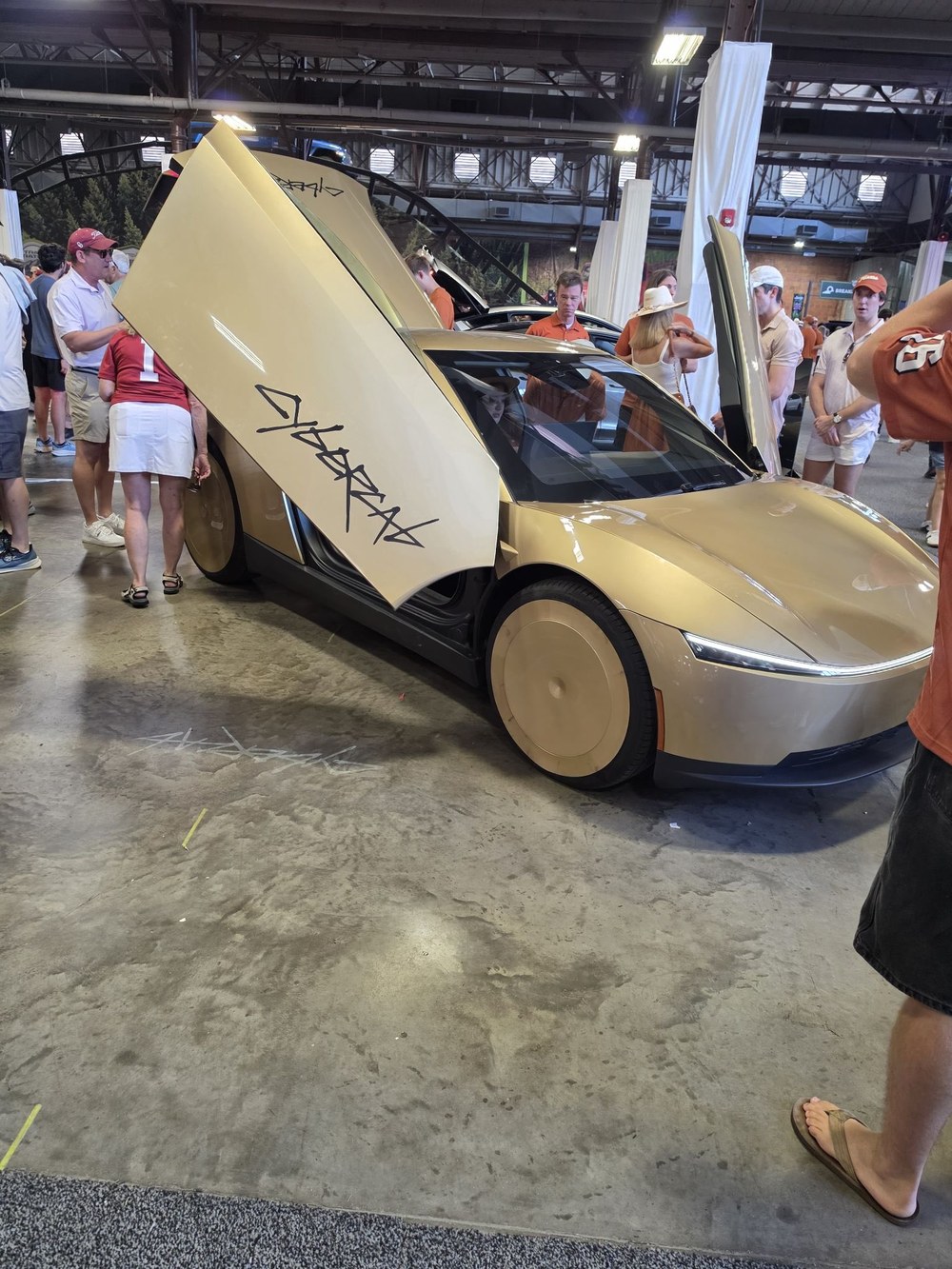 Gold Cybercab with doors open inside the Centennial Building at Fair Park. Photo via @thatdanielito / @RobotaxiRadar / X