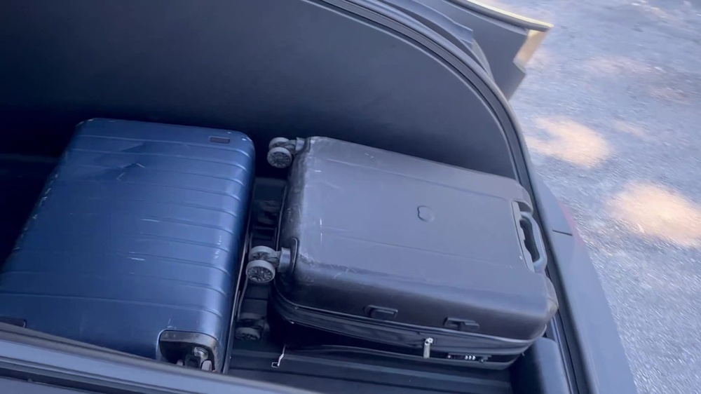 Open Cybercab trunk holding two hard-shell suitcases at the curb. Still via @BLKMDL3 / X