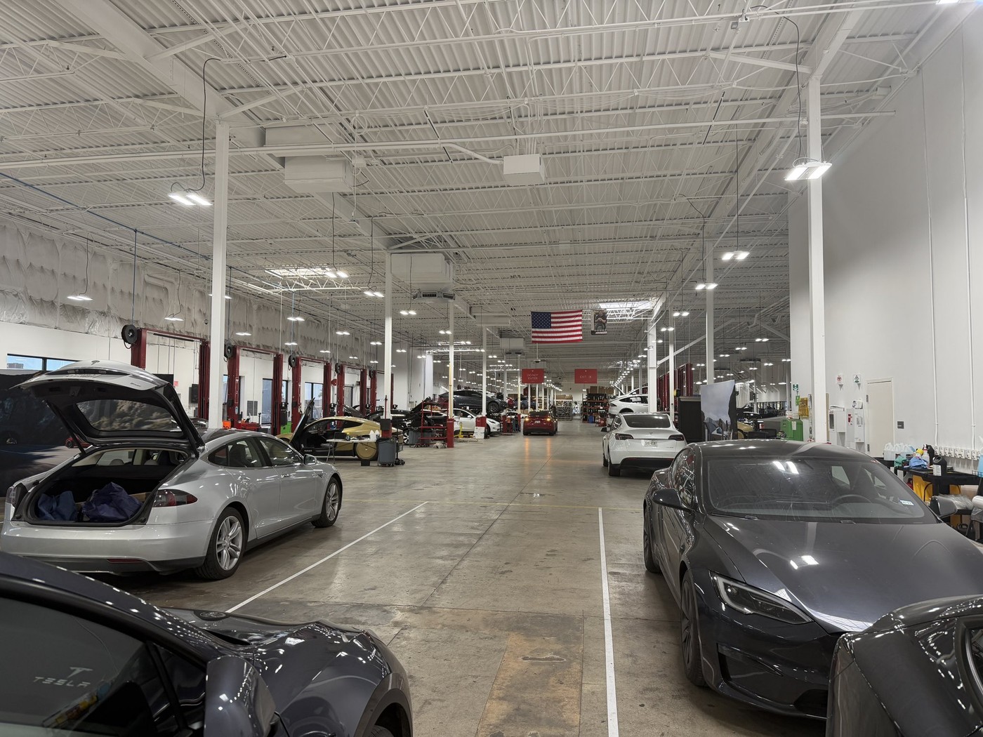 The Tesla service floor where the Cybercab was being repaired; the gold car sits in a bay at left. Image via @TeslaInvest2032 / X