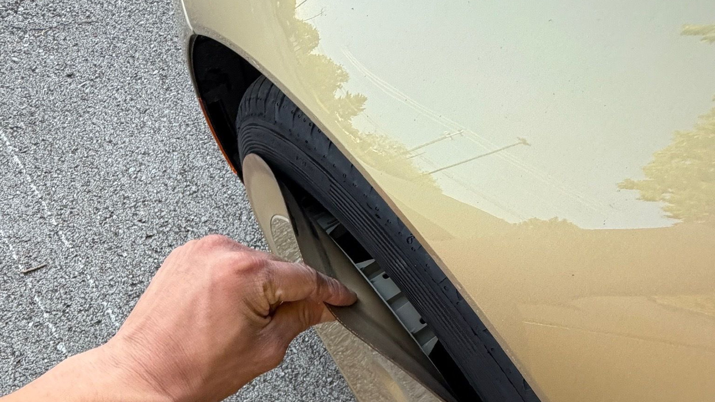 A hand peeling back the rubber outer lip of a gold Cybercab wheel cover, exposing the tire sidewall